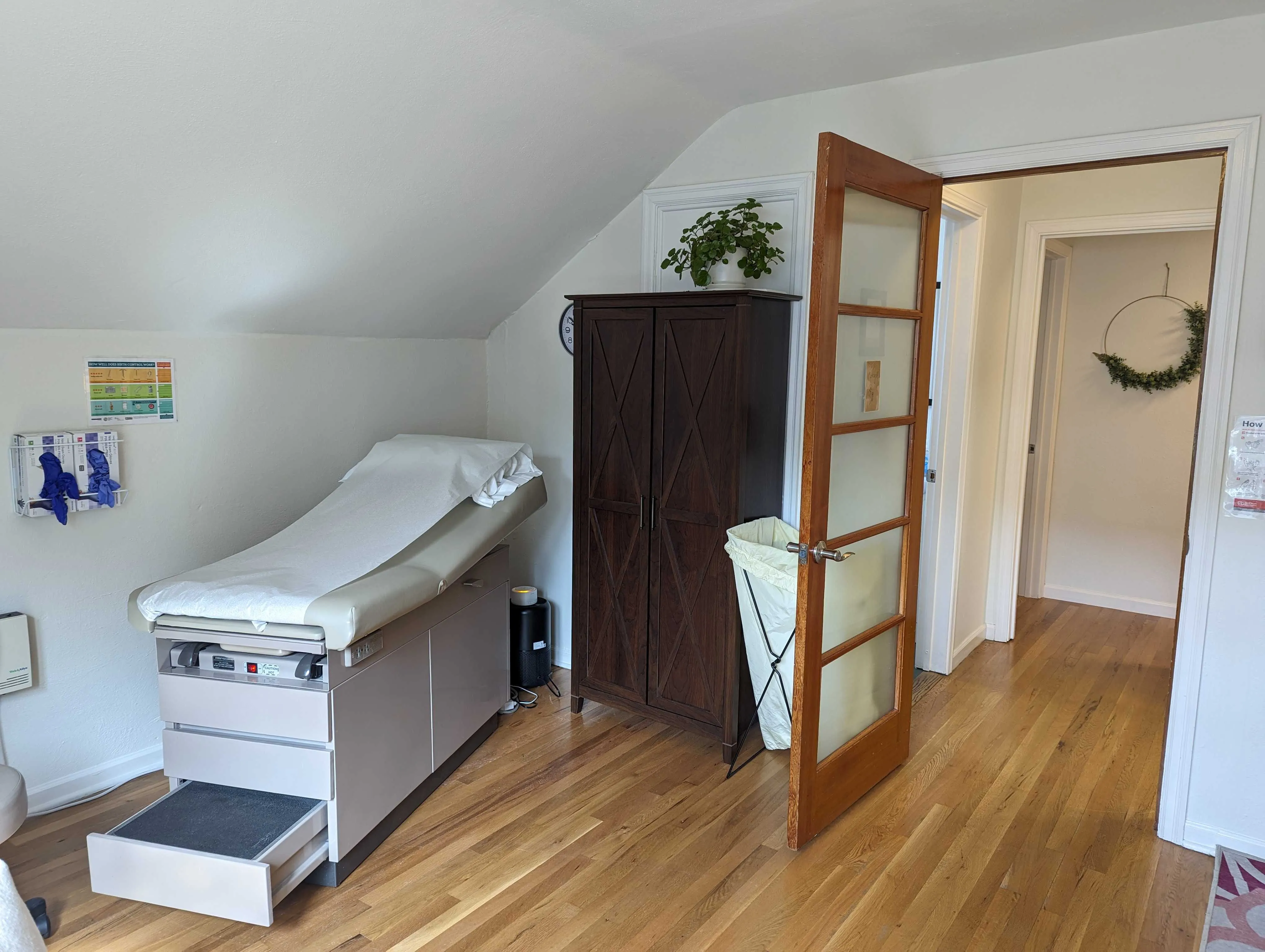 An exam room with an exam table, a wooden cabinet and a glass-panelled door