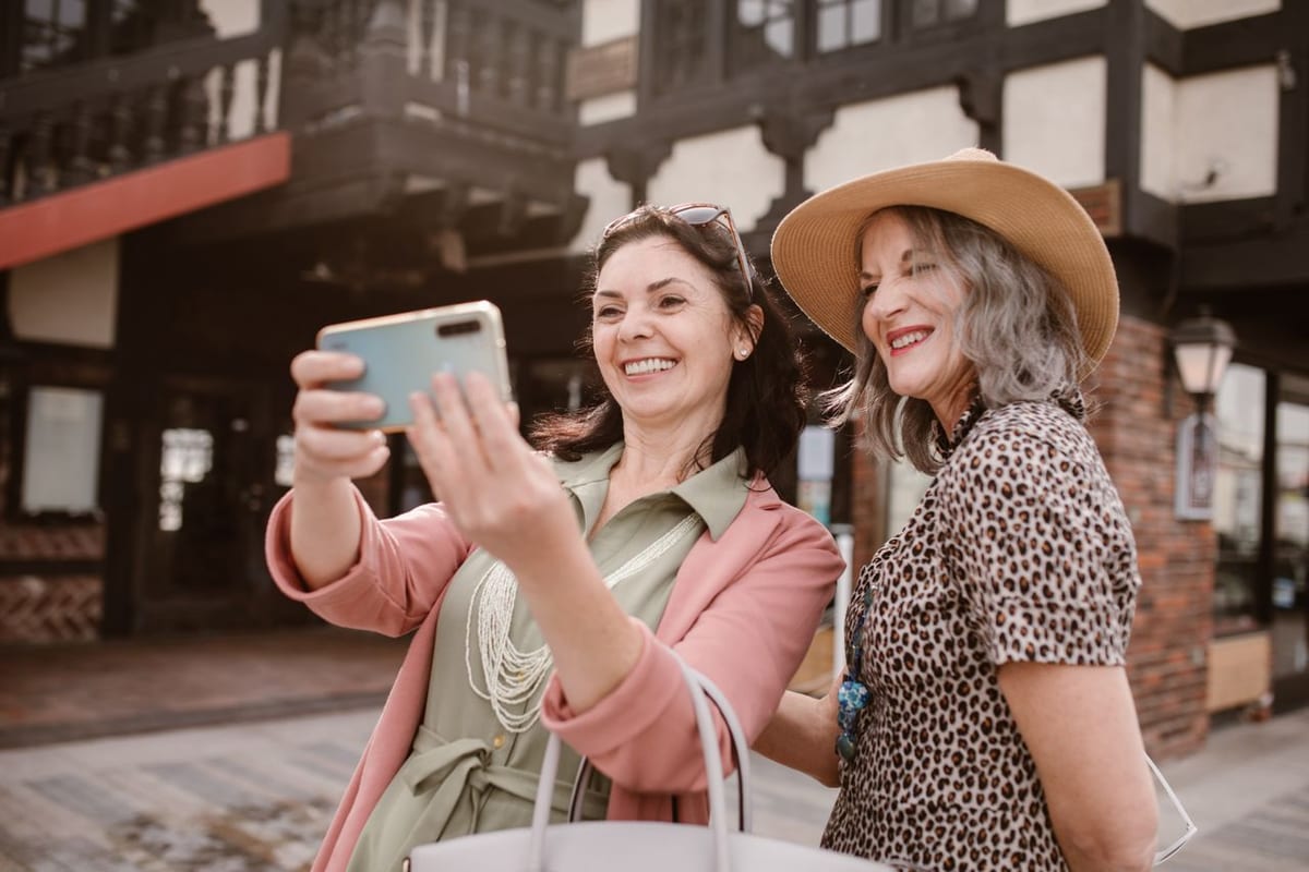 Two women in their fifties laughing as they take a selfie on a sunny street